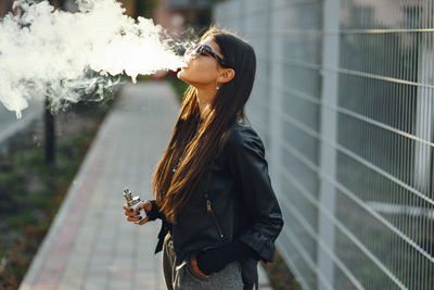 A Woman Vaping on a Footpath
