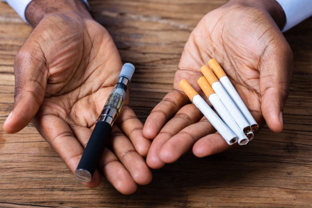 Hands holding a vape and cigarettes Hands holding both a vape and cigarettes to highlight the choice many people have to start quitting smoking