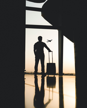 Man standing at airport window watching plane take off