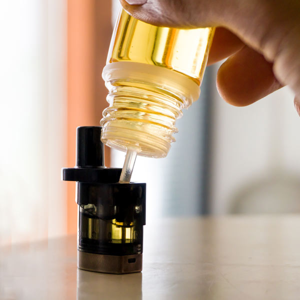 Person Filling a Vape Pod With Vape Juice Standing Upright on a Table