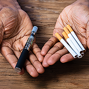 Man Holding Vape and Cigarettes in Both Hands